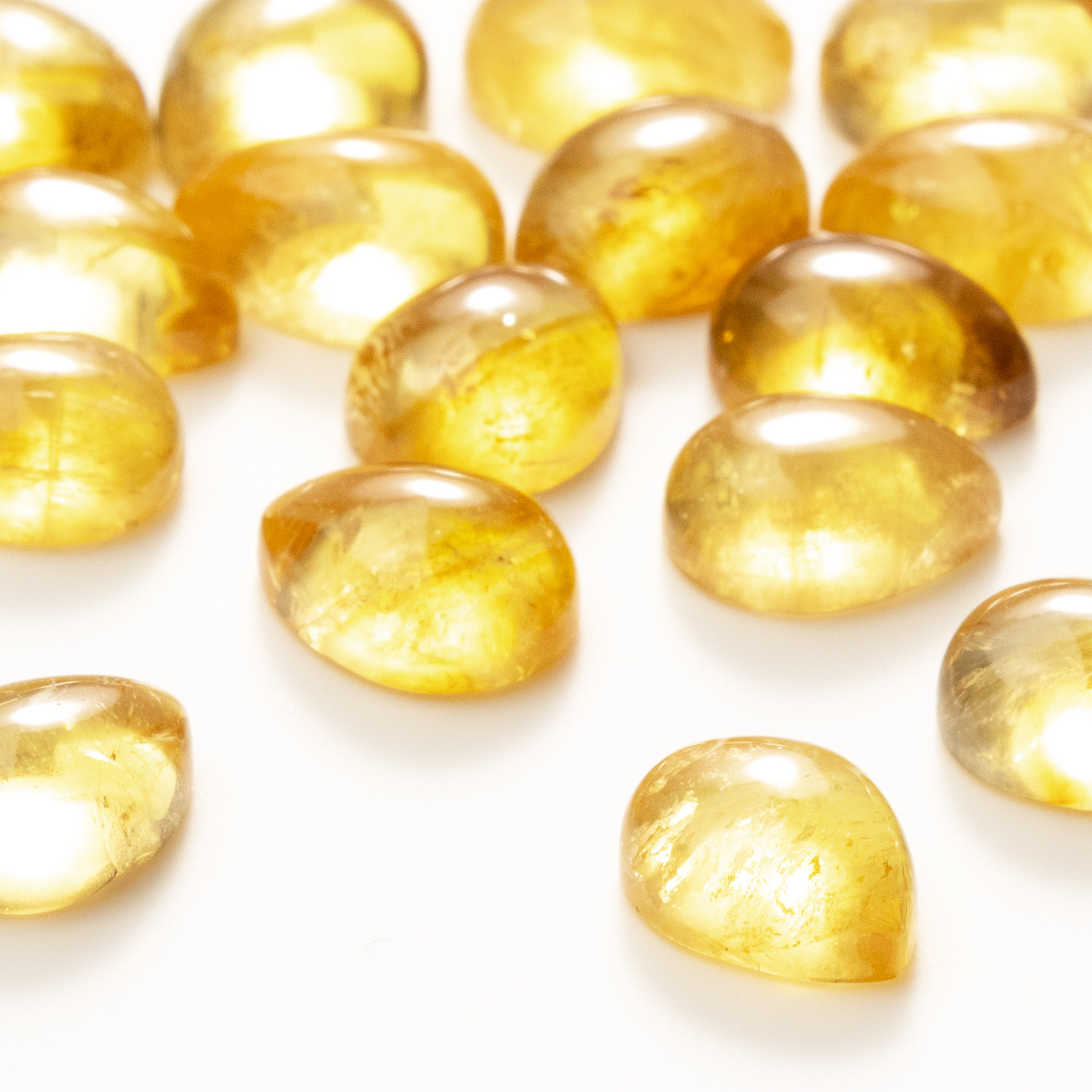 Orange-yellow coloured citrine teardrop cabochons placed on a white background