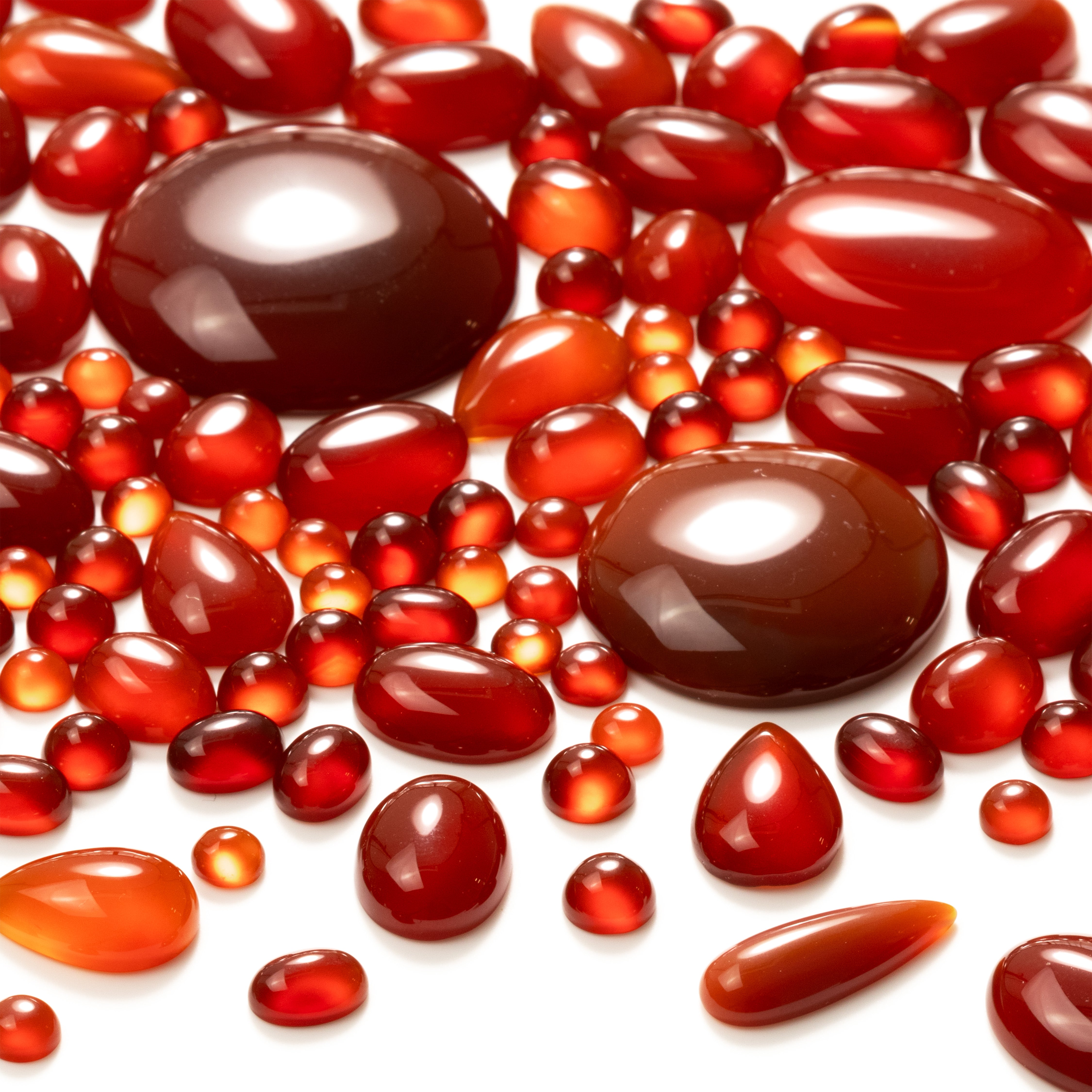 Carnelian cabochons, mixed shapes and sizes, scattered on a white background