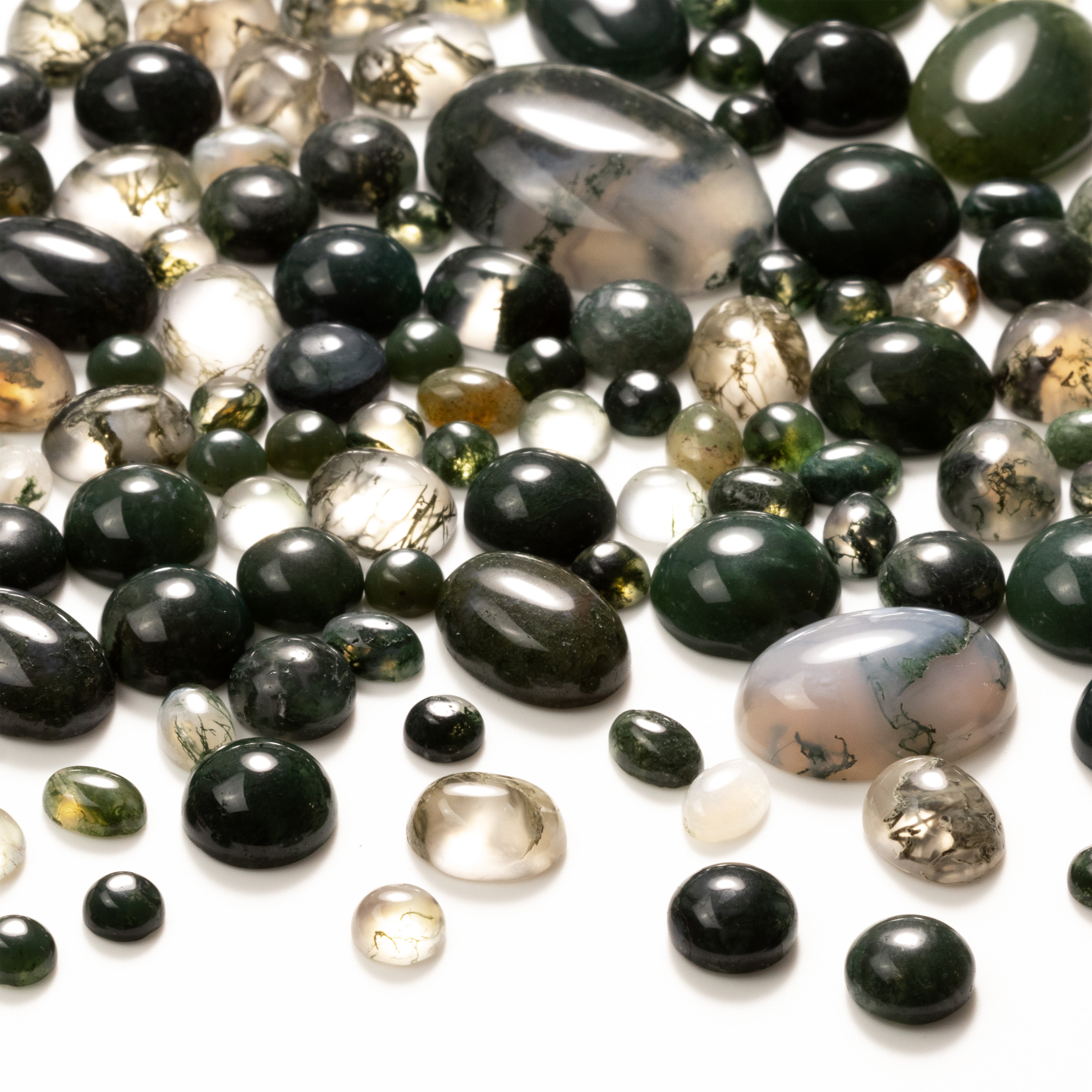 Green moss agate cabochons, oval and round shapes, scattered on a white background