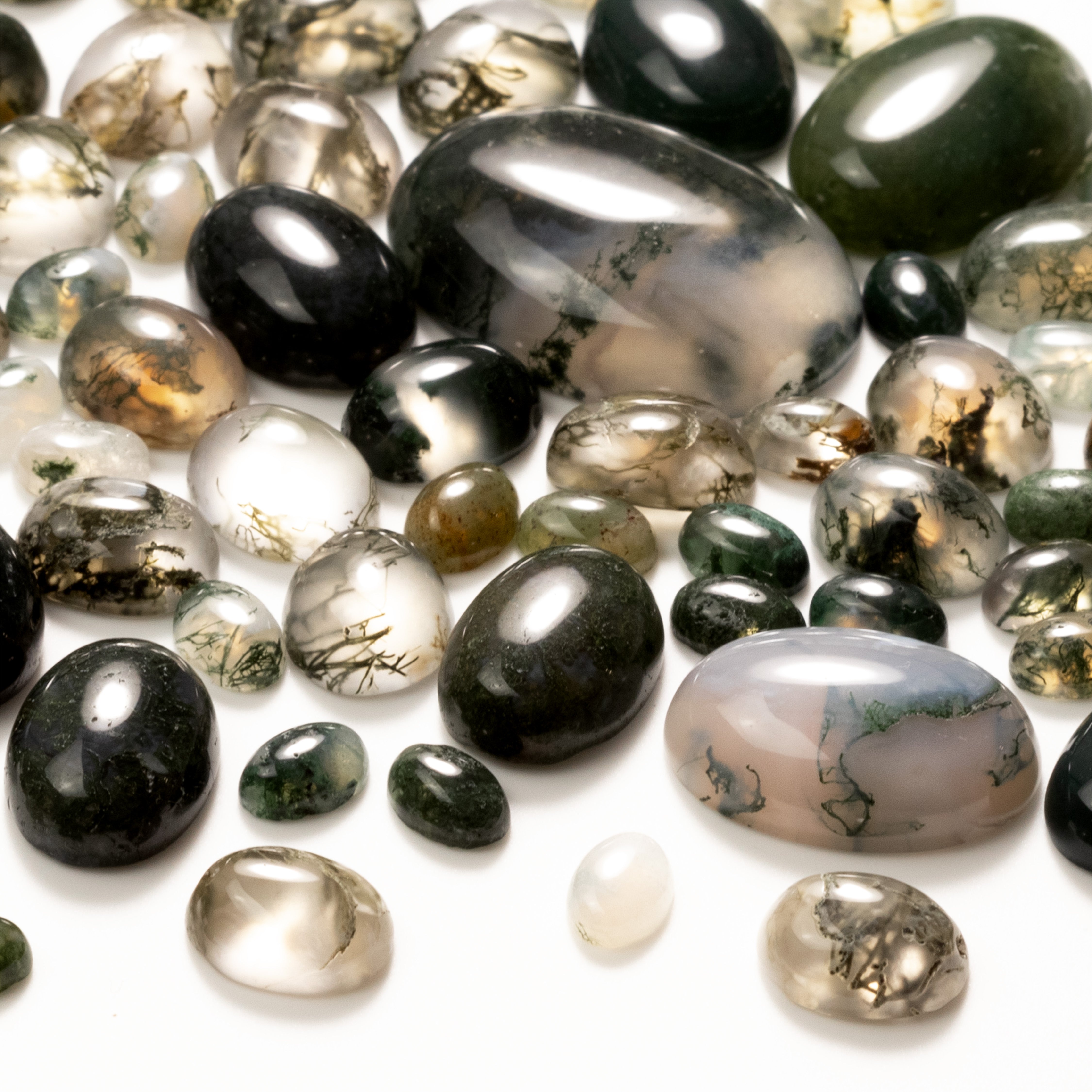 Green moss agate oval cabochons scattered on a white background
