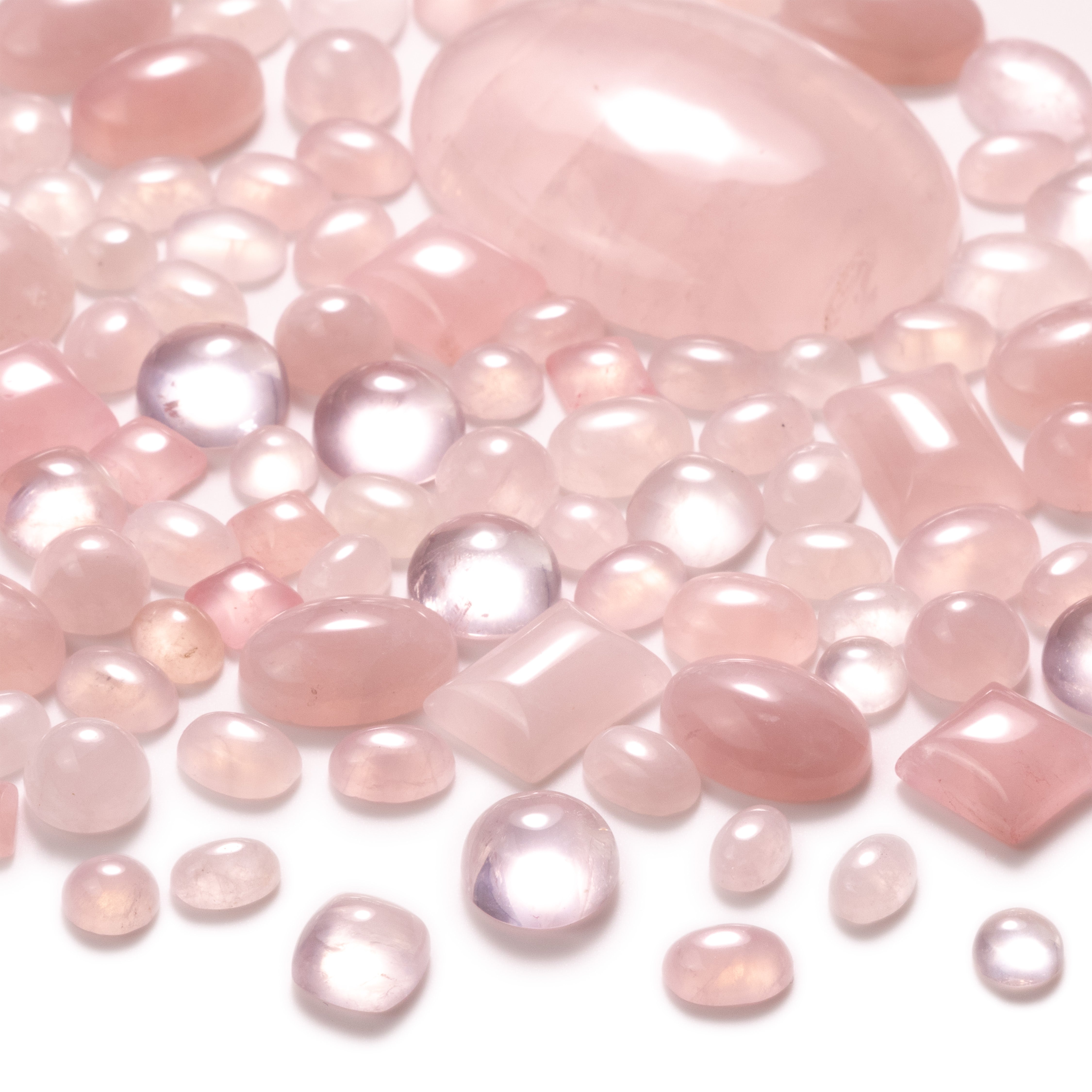 Rose Quartz cabochons, mixed shapes and sizes, scattered on a white background
